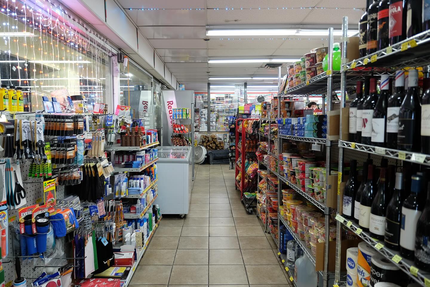 Corner store aisle with shelves of bottles and a lit window of goods