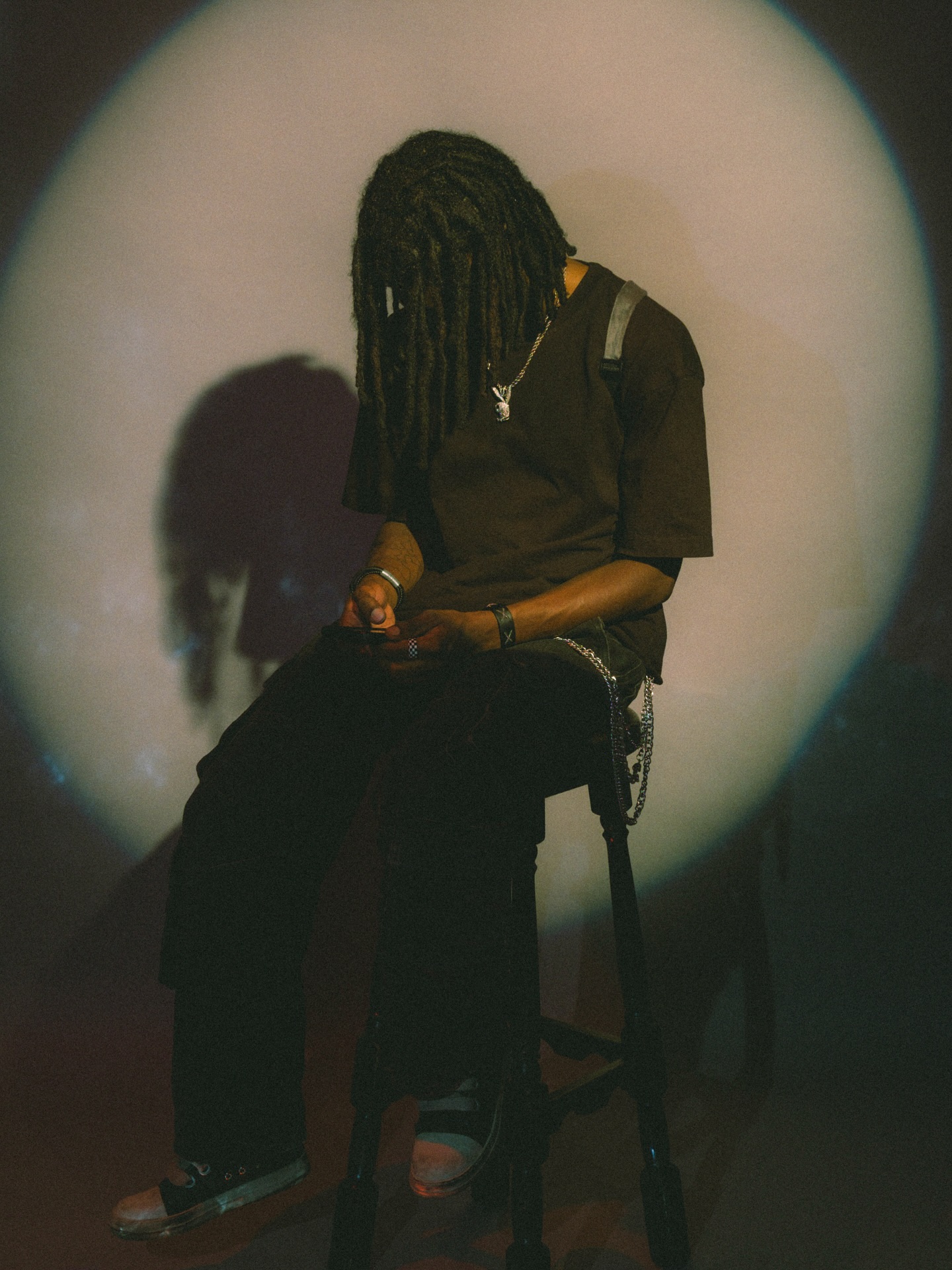 Person seated on a stool inside a circle of light, head bowed