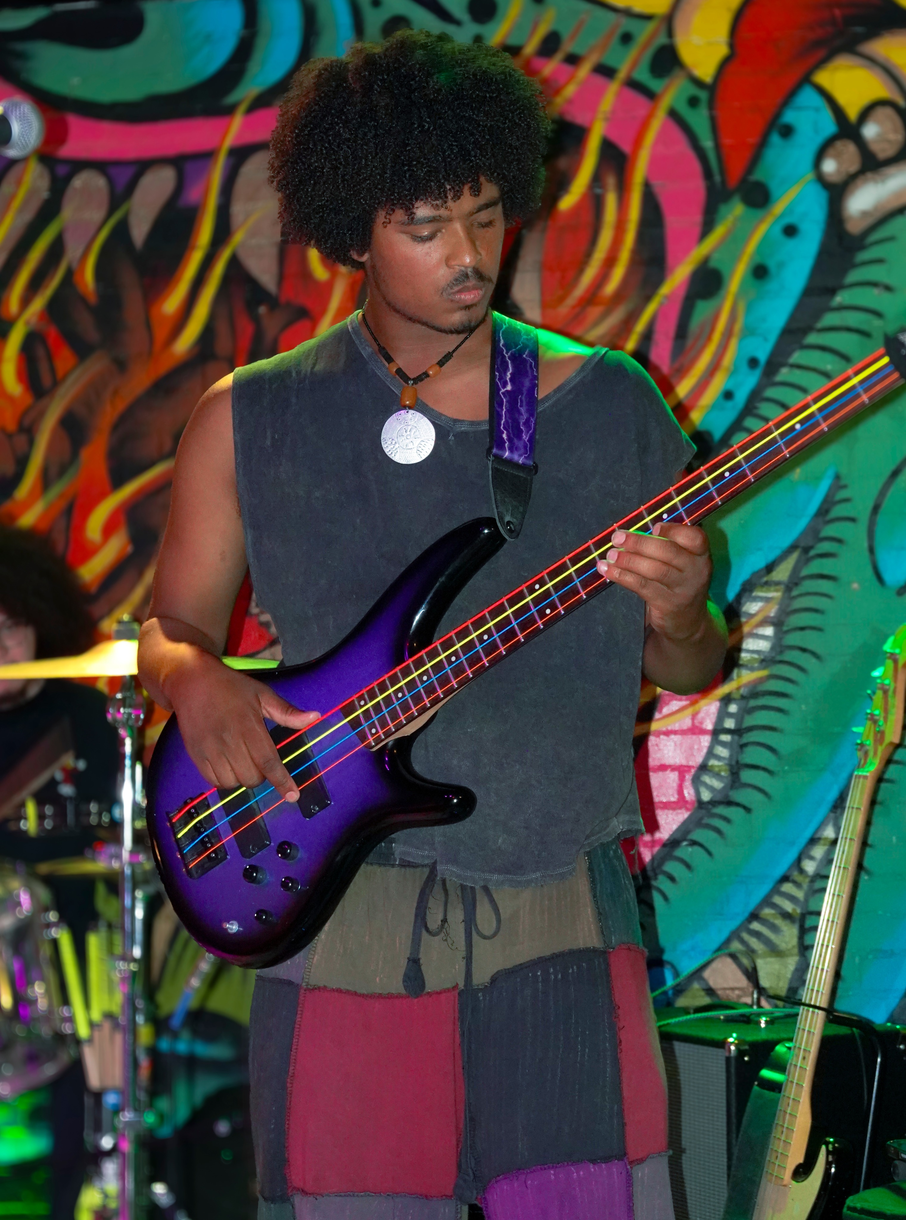 Bassist playing a purple bass against a colorful painted mural